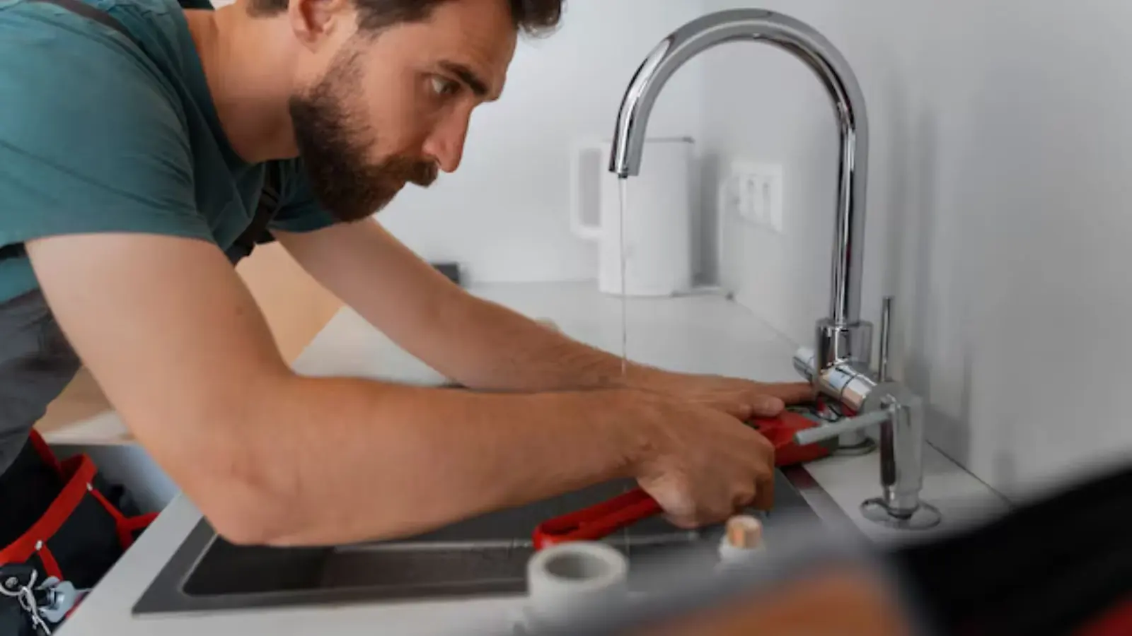 Plumber leaning over a kitchen sink with a wrench to repair a faucet